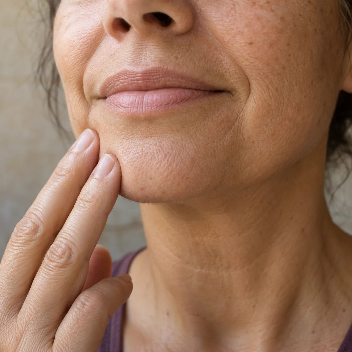 An illustrative natural-skin close-up of a mature woman gently touching her cheek and chin