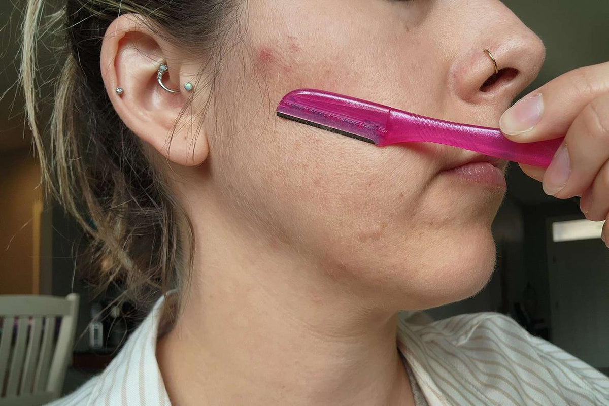 Woman using a pink facial razor on her cheek